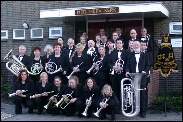 Het orkest op de trappen voor de kerk, met instrumenten en het verenigingsvaandel.